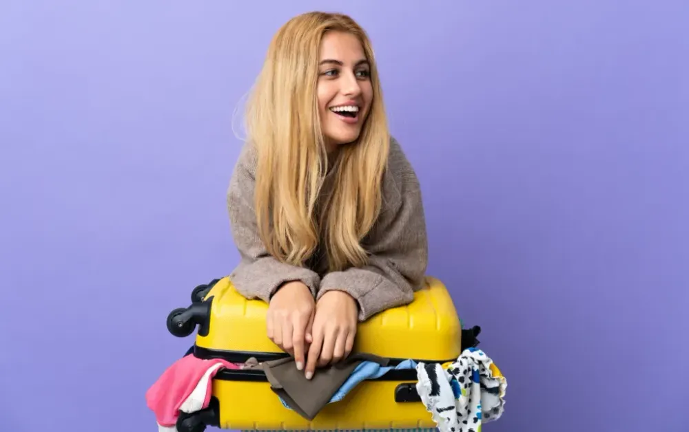 Person holding a yellow suitcase closed on a purple background